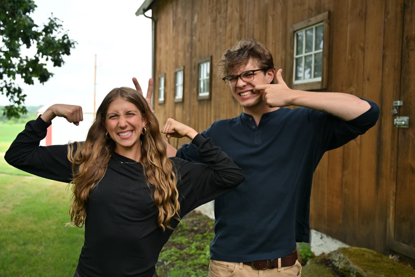 Two people flexing and laughing in front of the barn