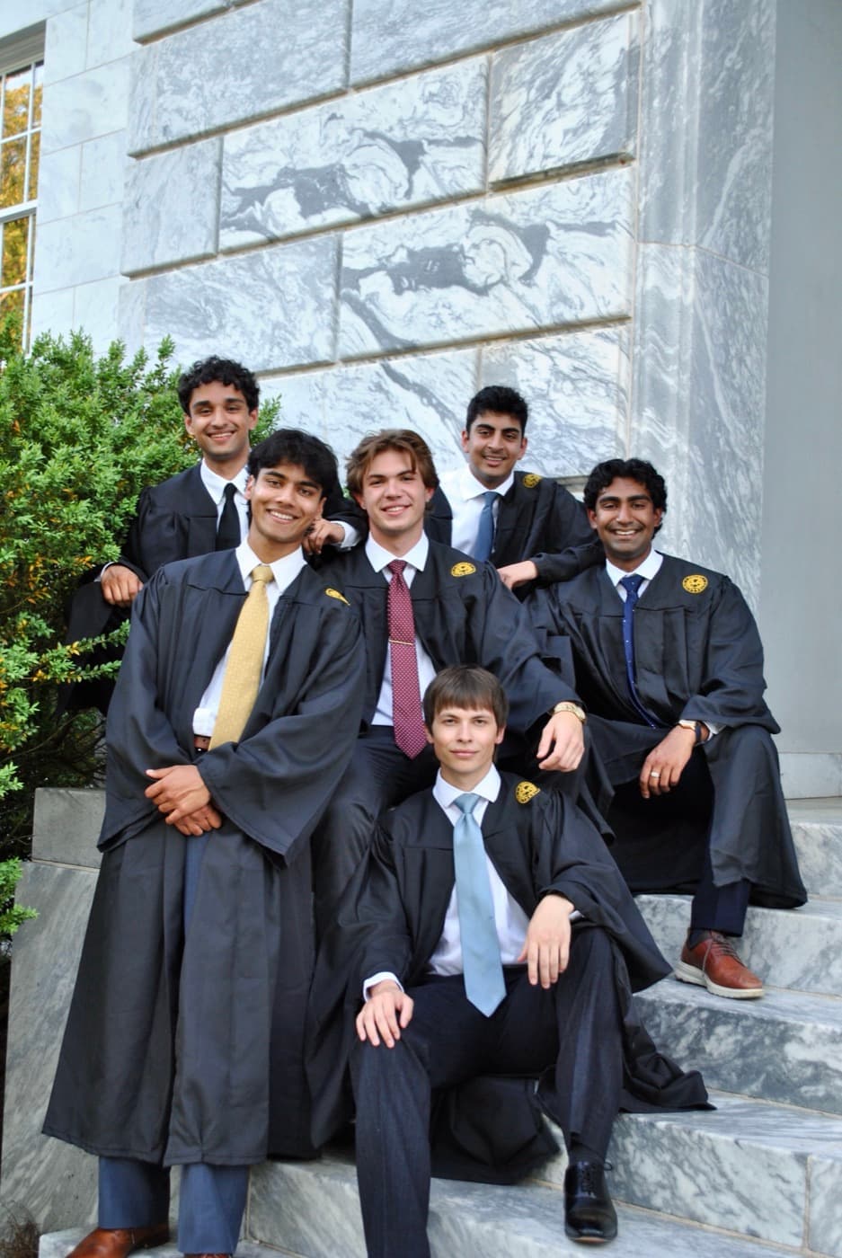 Six graduates in gowns posed on marble steps