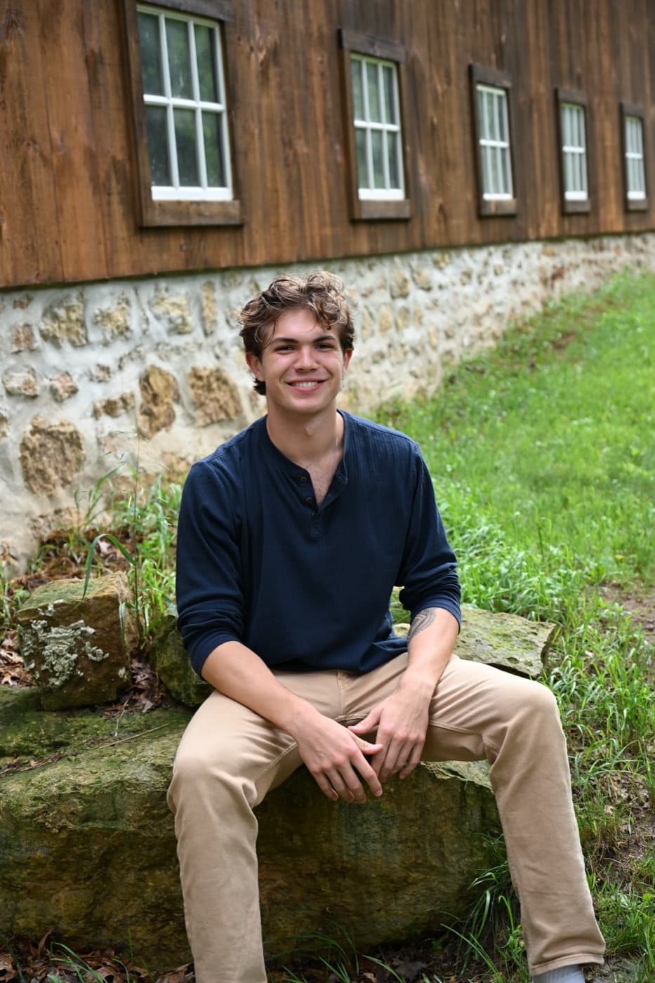 Sam sitting on a rock in front of a barn, smiling