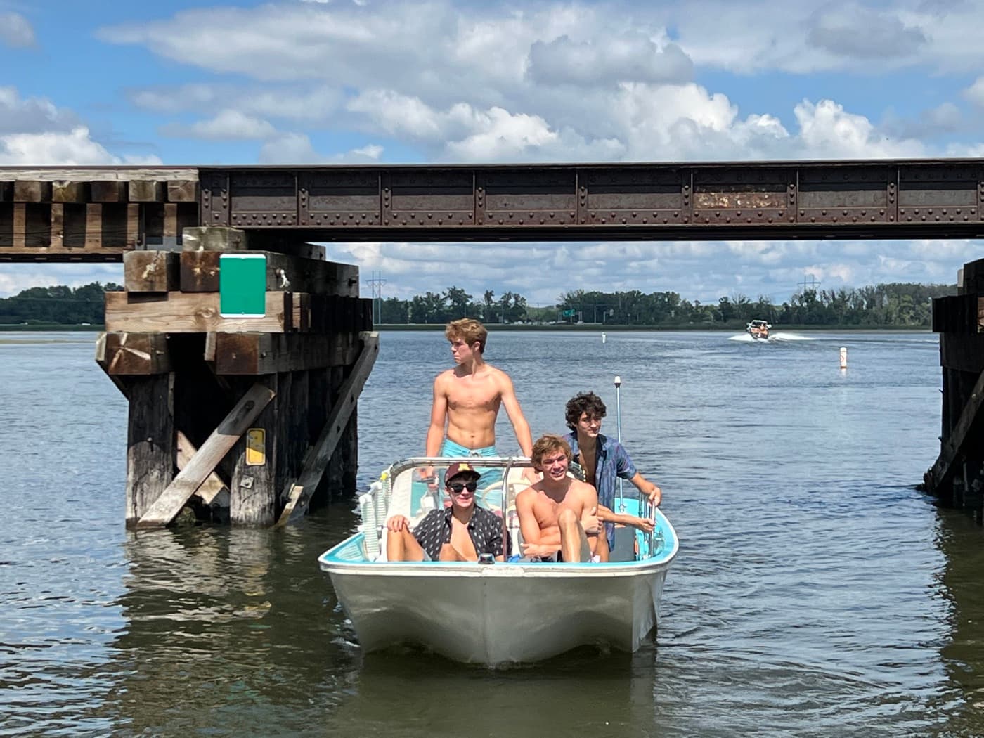 Friends in a small motorboat under a railroad bridge